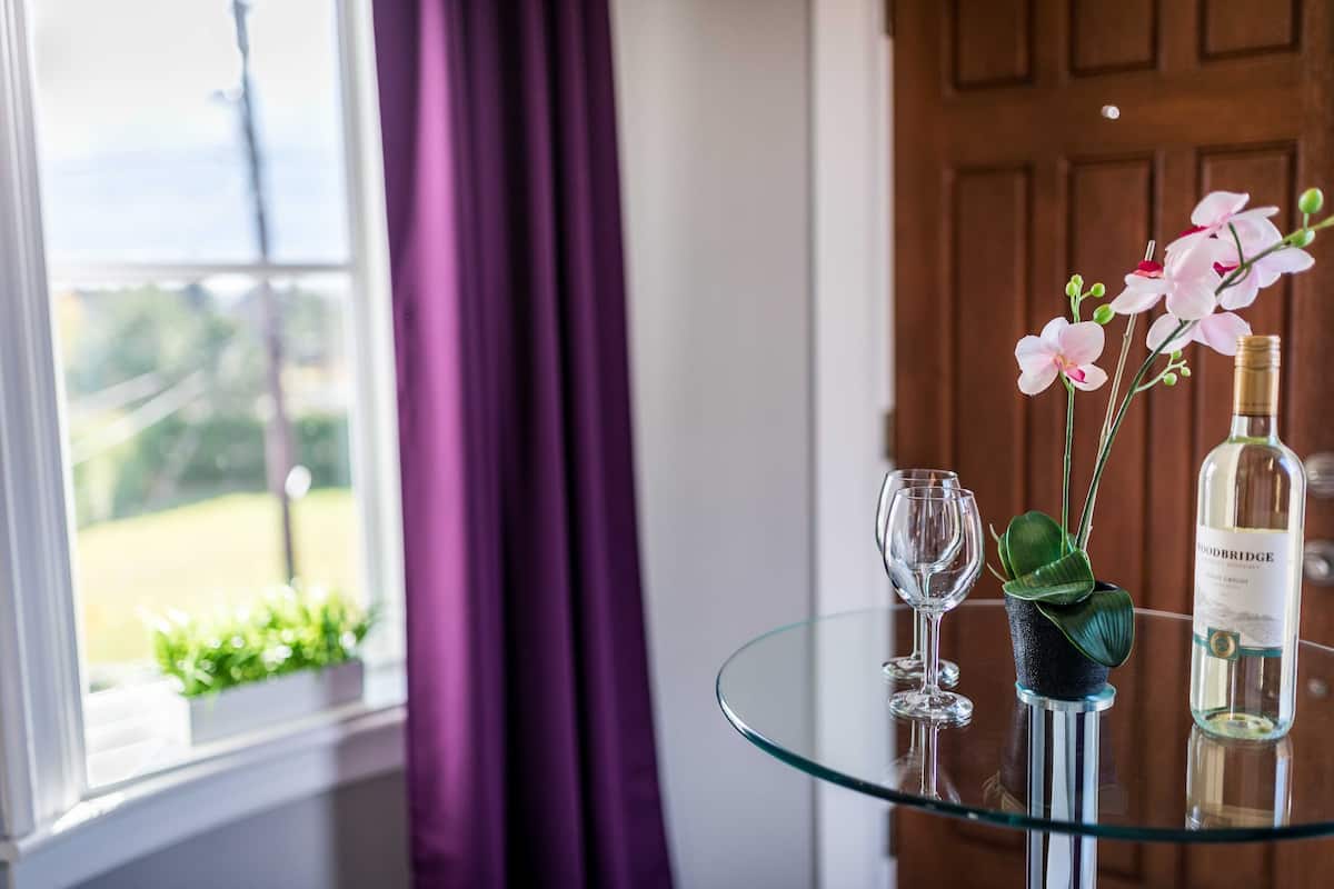 Een glazen tafel met een fles wijn, een glas en een bloempot.