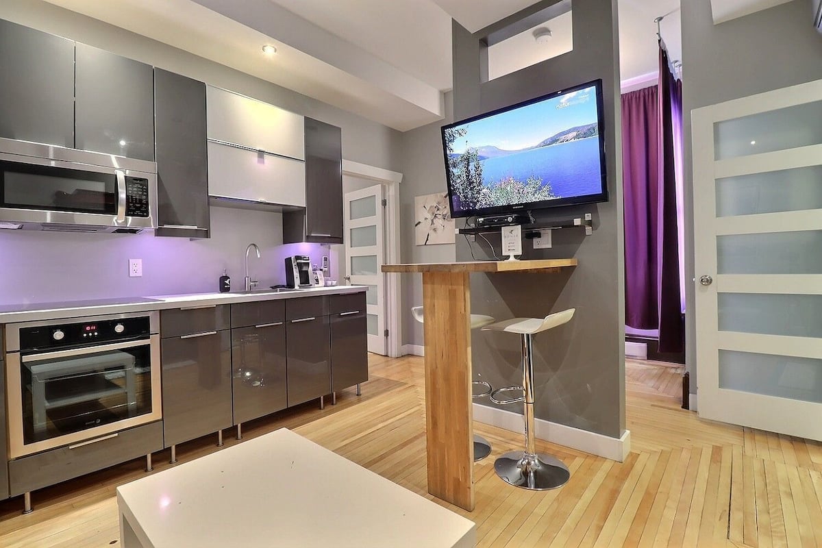 Een moderne keuken met roestvrijstalen apparatuur, een flatscreen televisie aan de muur en een houten kruk.