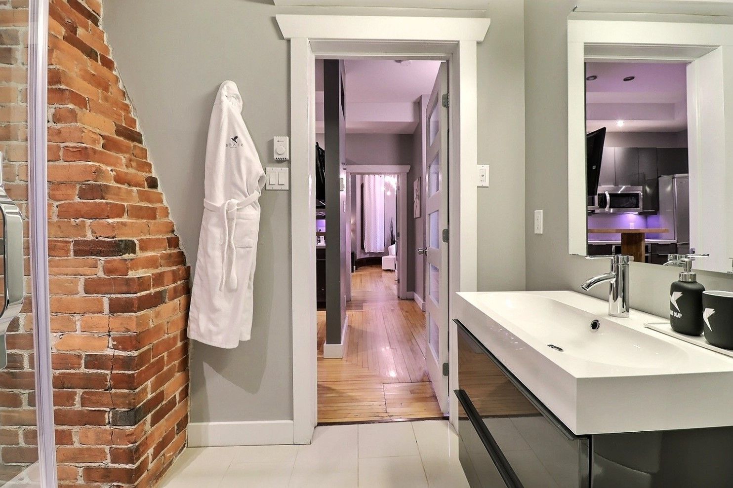 A modern bathroom with a large mirror, white sink, and a robe hanging on the wall.