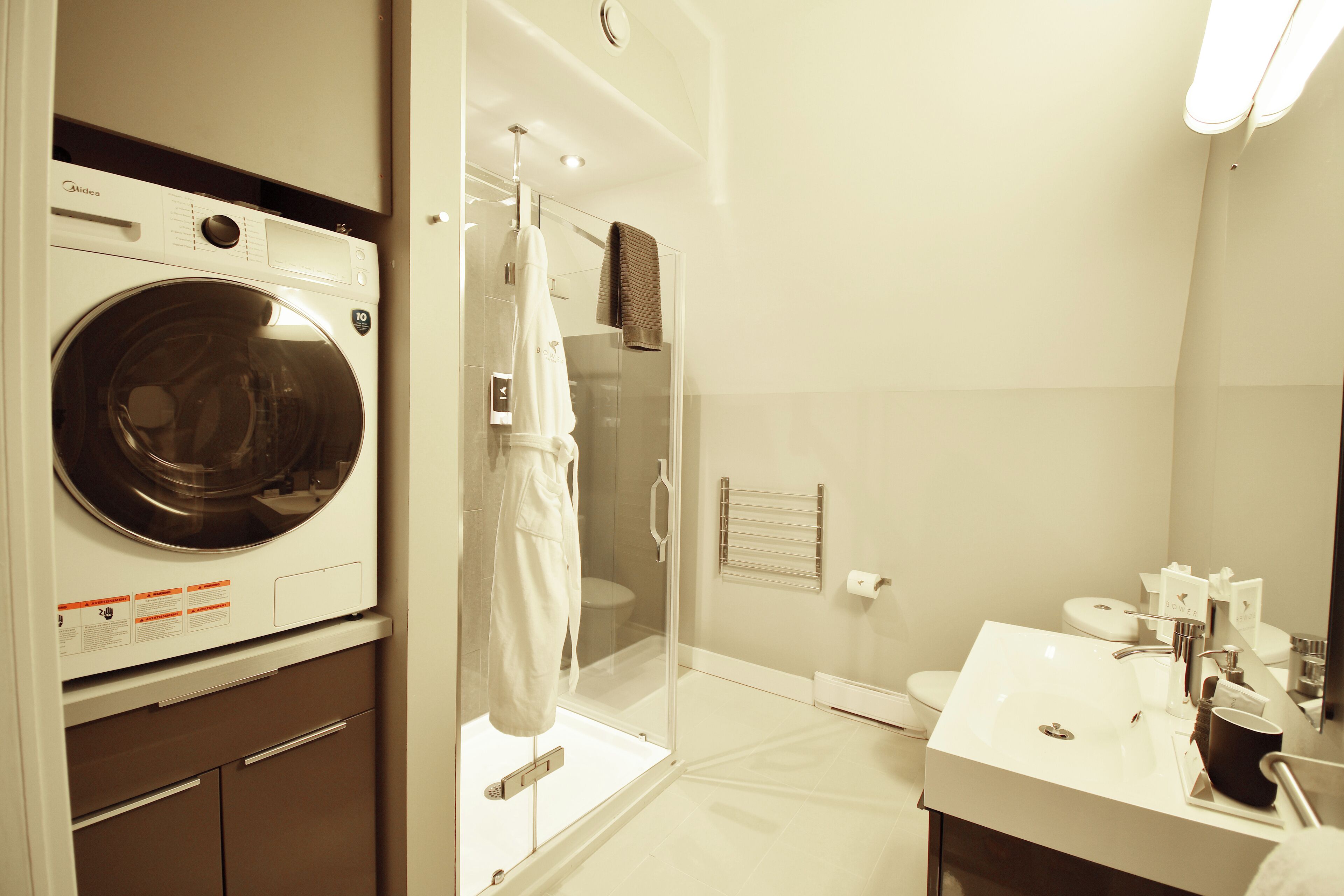 Une salle de bain d’hôtel équipée d’un lave-linge, d’une douche en verre et d’un lavabo avec des articles de toilette.