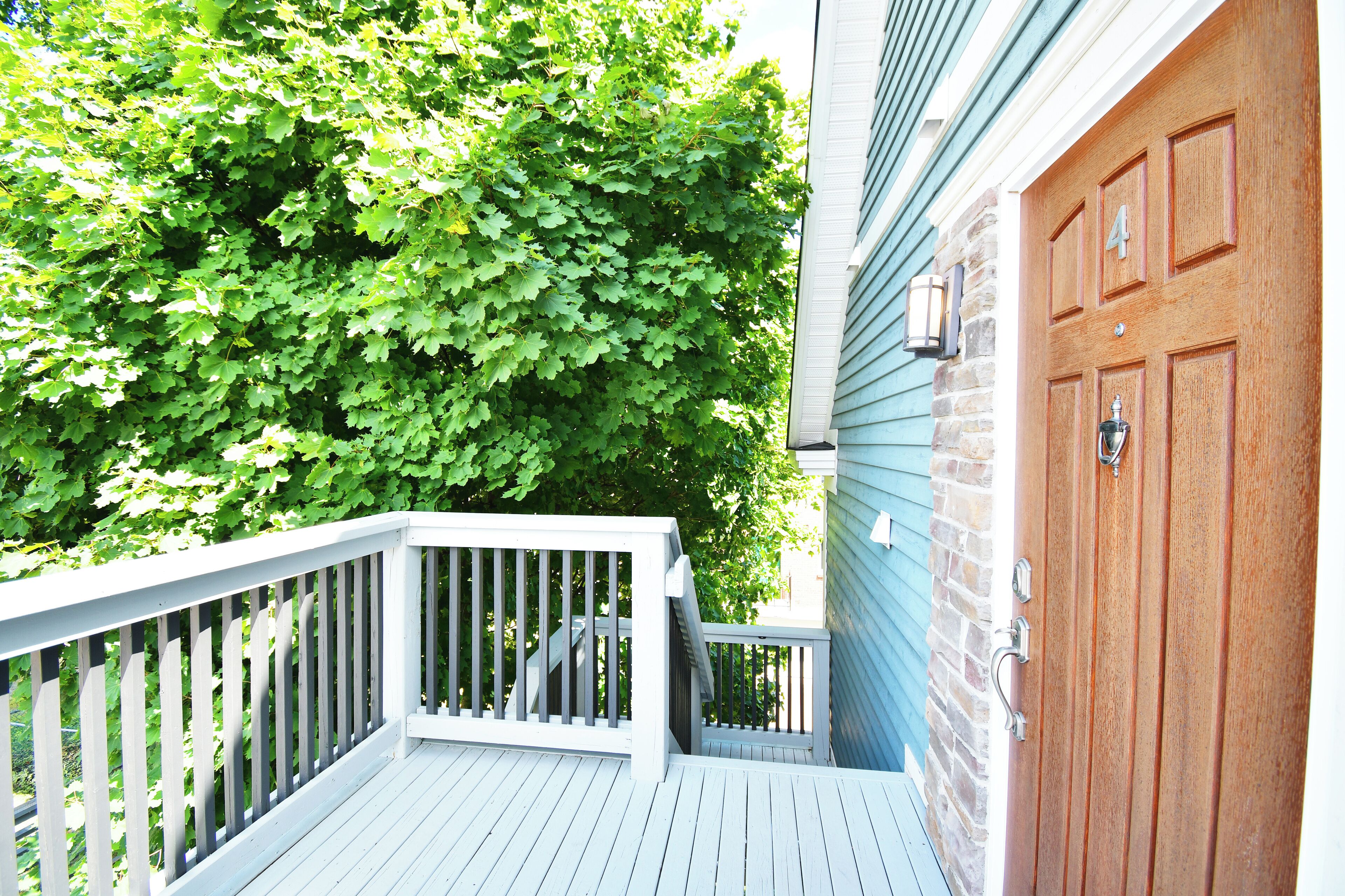 A wooden deck with a white railing, a brick wall, and a blue house with a brown door.