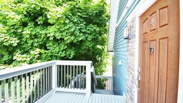 A wooden deck with a white railing, a brick wall, and a blue house with a brown door.