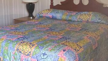 A bed with a colorful quilt, a wooden headboard, a bedside lamp, and a striped wall.