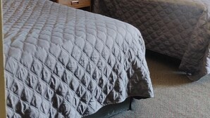 Hotellihuone, jossa on kaksi sänkyä, yöpöytä valaisimineen ja seinällä oleva kehystetty kuva.