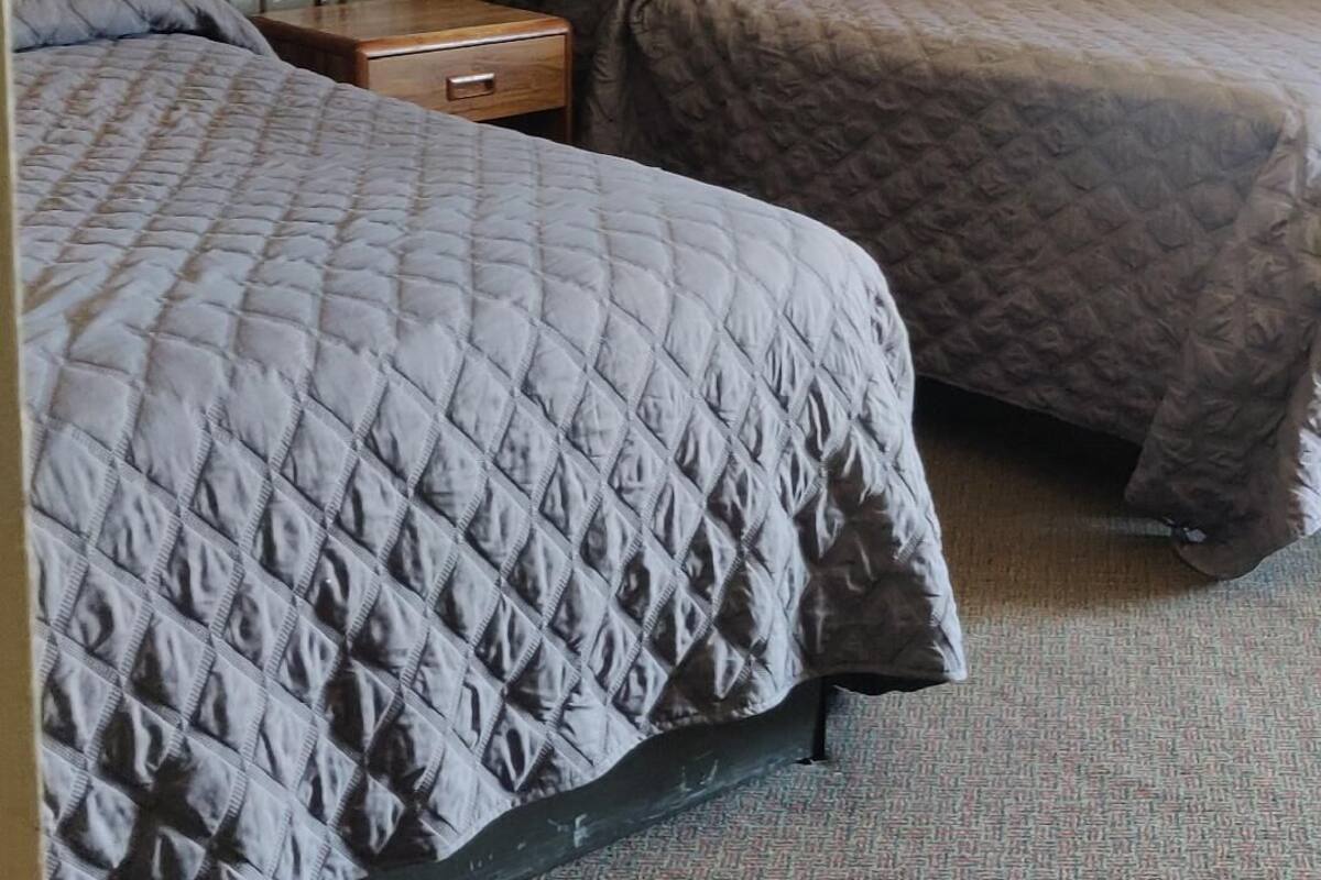 A hotel room with two beds, a nightstand with lamps, and a framed picture on the wall.