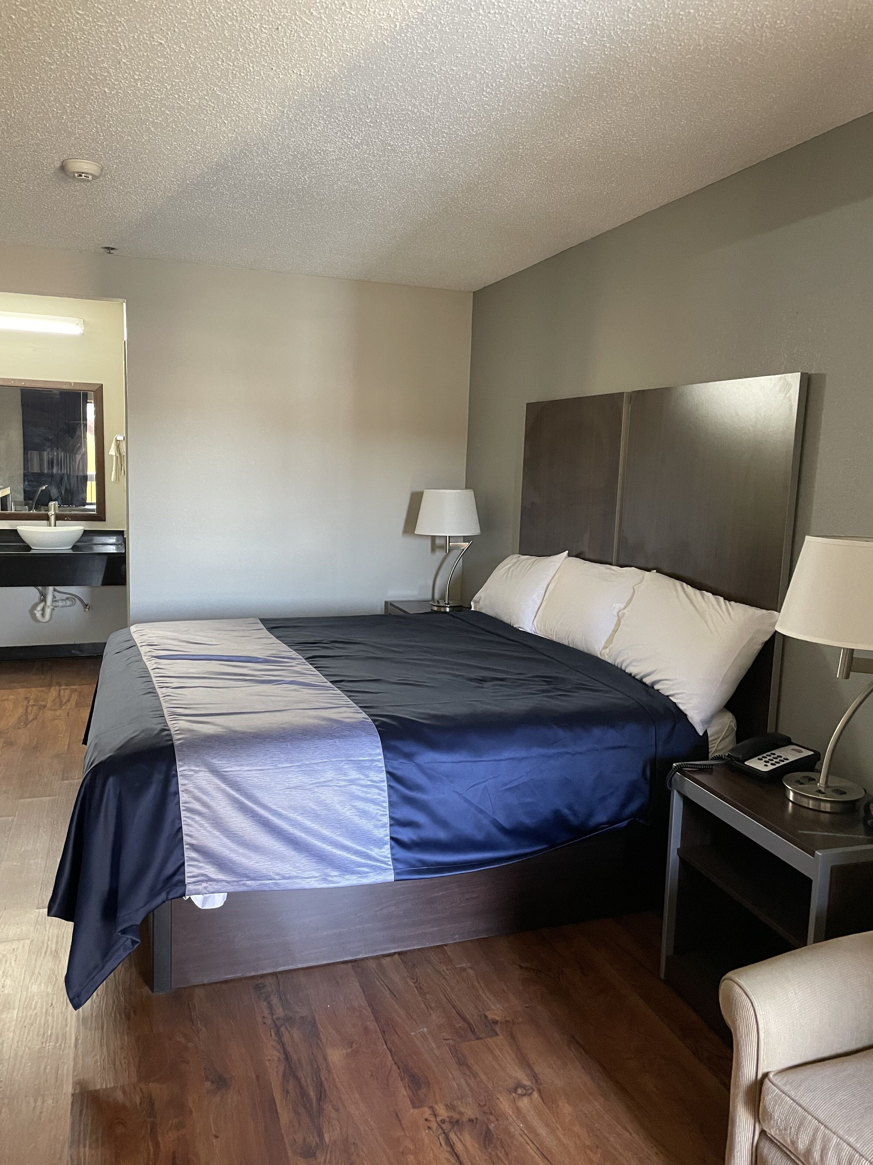 Una habitación de hotel con cama, mesitas de noche, un espejo y baño con lavamanos e inodoro.