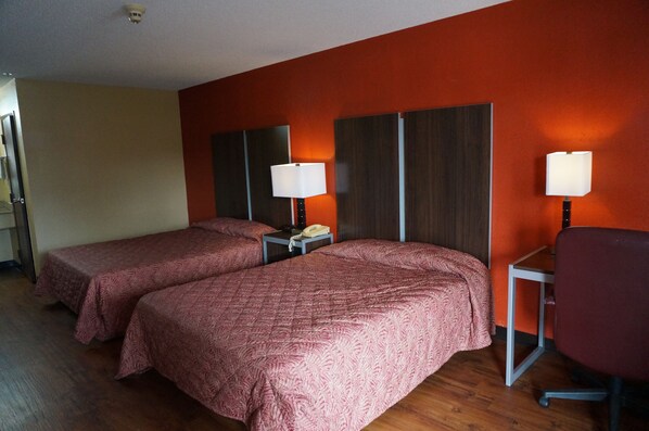 A hotel room with two beds, each with a patterned bedspread, bedside lamps, and a small table with a telephone.