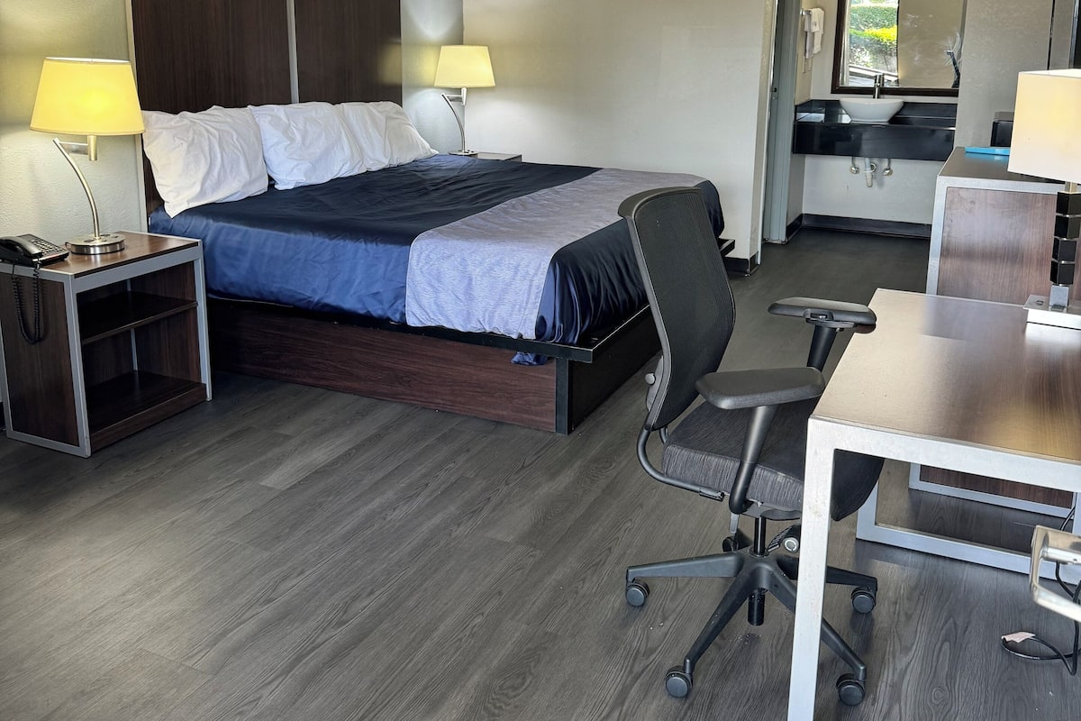A hotel room with a bed, desk, chair, and a bathroom visible through an open door.