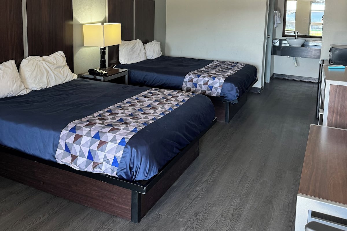 A hotel room with two beds, a desk, and a kitchenette.