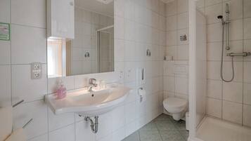 Un baño con lavamanos blanco, espejo, inodoro y zona de ducha.