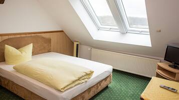 Quarto com cama, televisão e claraboia.