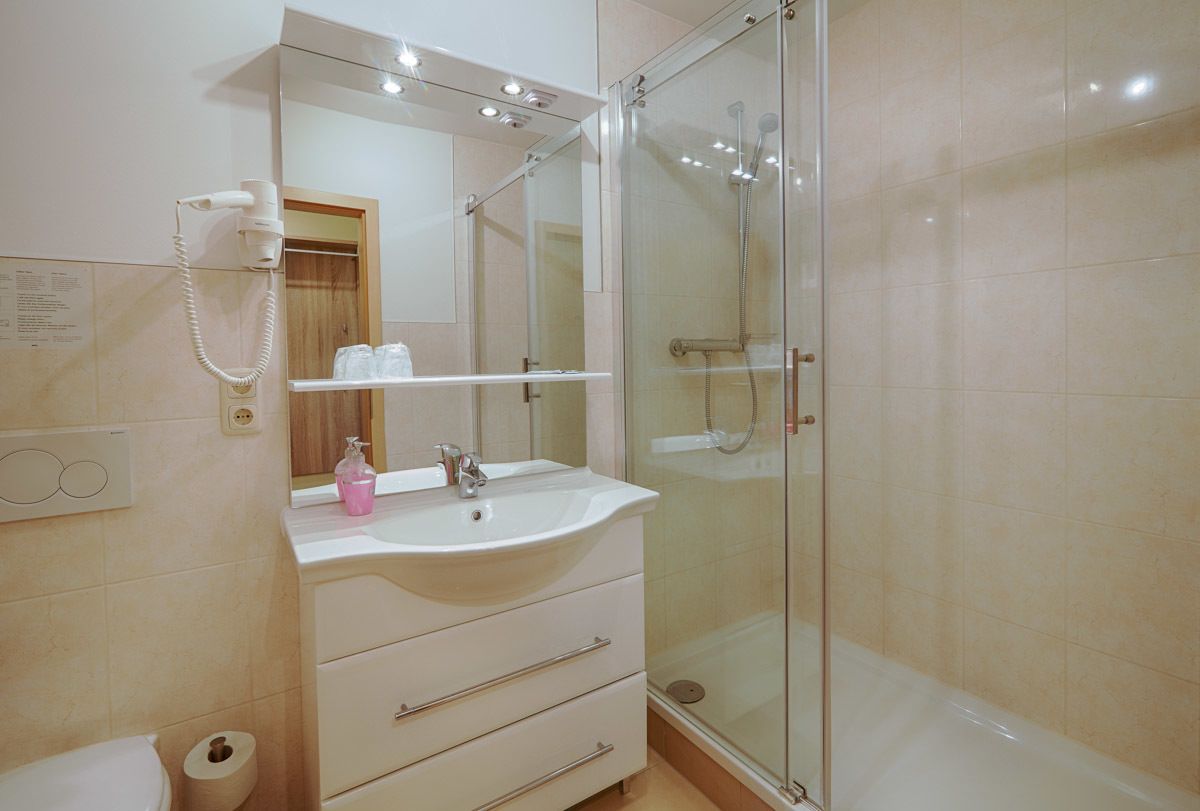 Un bany modern amb dutxa tancada amb vidre, un lavabo blanc i un mirall a sobre.