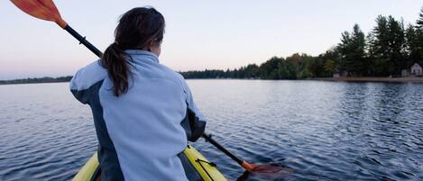 A person kayaking on a calm lake with a forested shoreline in the background.