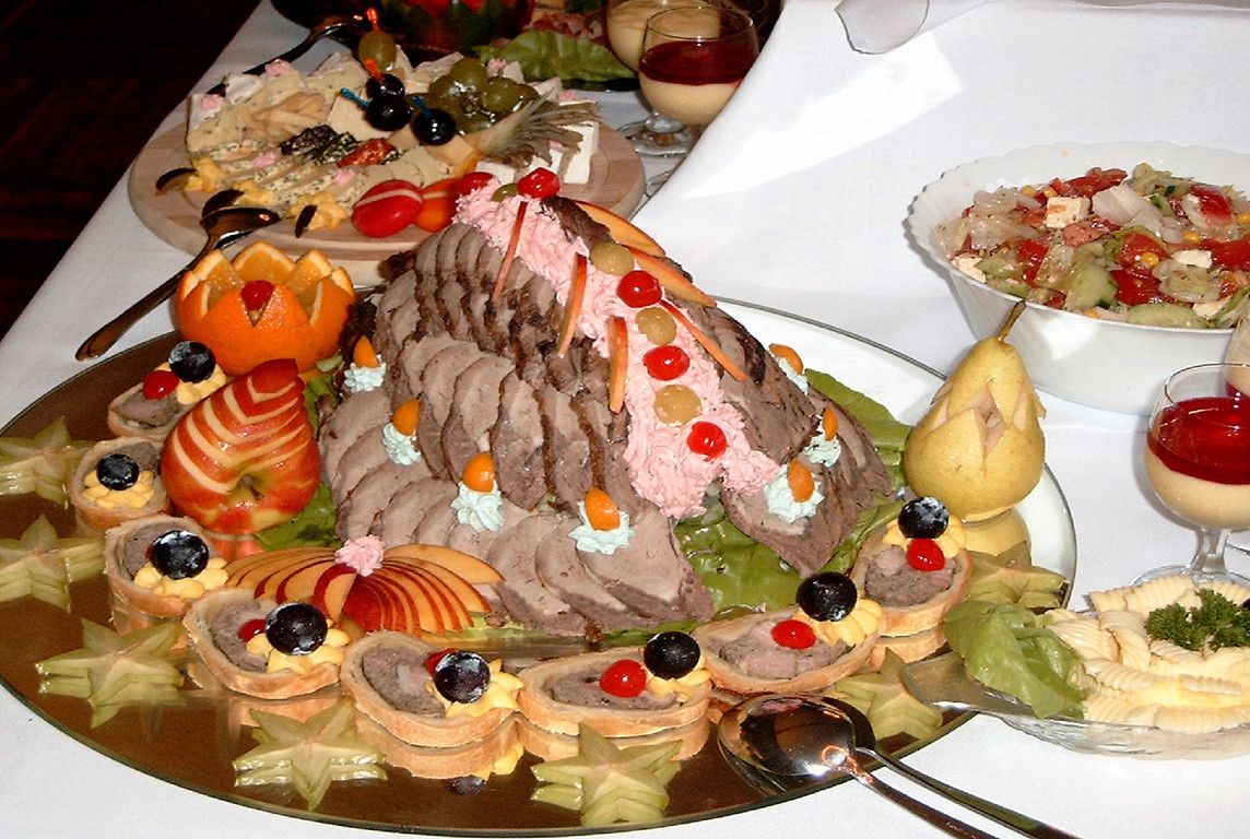 A large, ornate meat centerpiece with various garnishes and side dishes on a table.