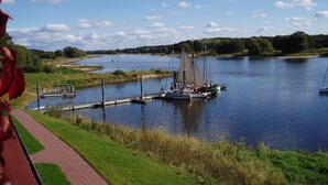 Vista del río con barcos amarrados, un sendero para caminar y una zona verde.