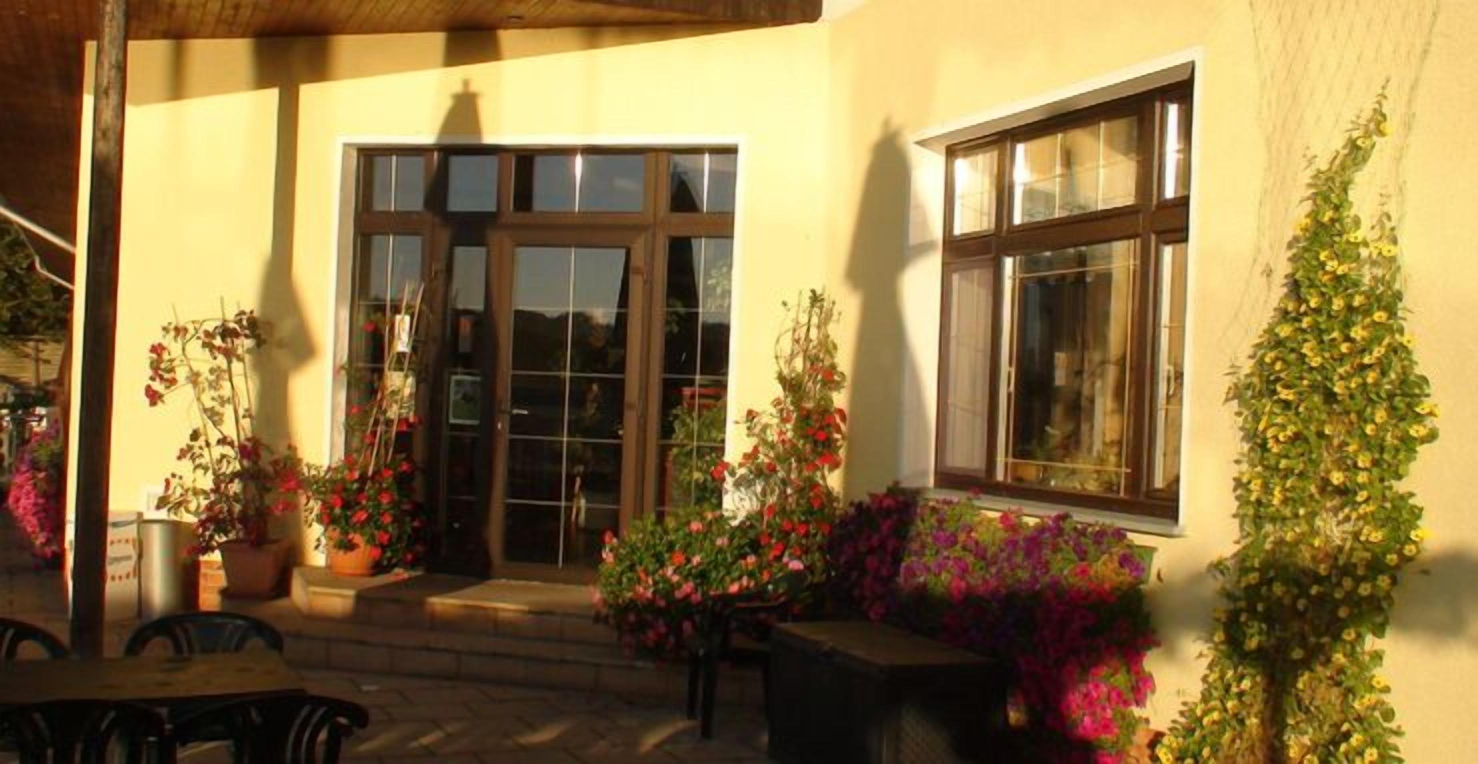 A building with a large glass door and windows, surrounded by potted plants and flowers.