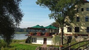 Un edificio junto al lago con una pequeña entrada, un área de estar al aire libre cubierta y un sendero que conduce a la entrada.