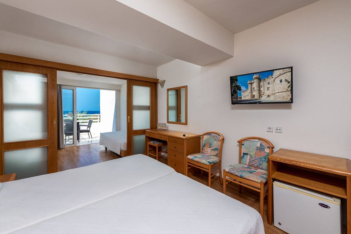 A bedroom with a bed, a desk, two chairs, a small fridge, and a painting on the wall.