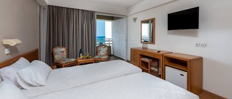A hotel room with a bed, a desk, a chair, a dresser, a television, and a view of the ocean.