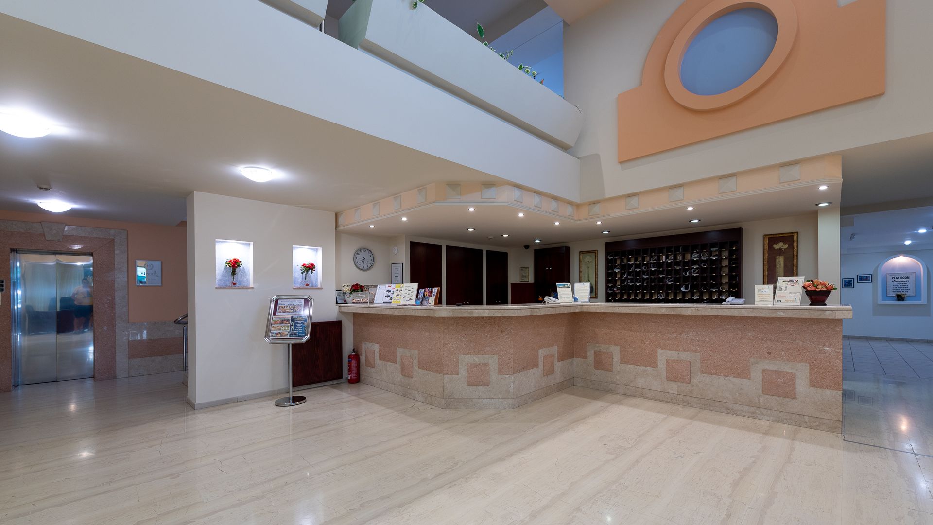 Un hall d’hôtel avec un sol en marbre, un comptoir d’accueil, une horloge et un présentoir à chaussures.