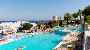 Una gran piscina al aire libre con varias pistas, rodeada de tumbonas y sombrillas, y vistas al mar.