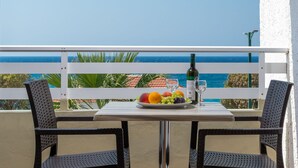 Un balcón con una mesa para dos personas, con un plato de fruta, una botella de vino y una copa.