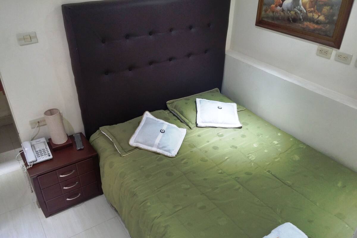 A neatly made bed with a green bedspread, two pillows, and a folded towel.