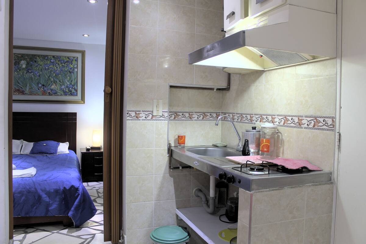A hotel room with a bed, a small kitchenette, and a bathroom.