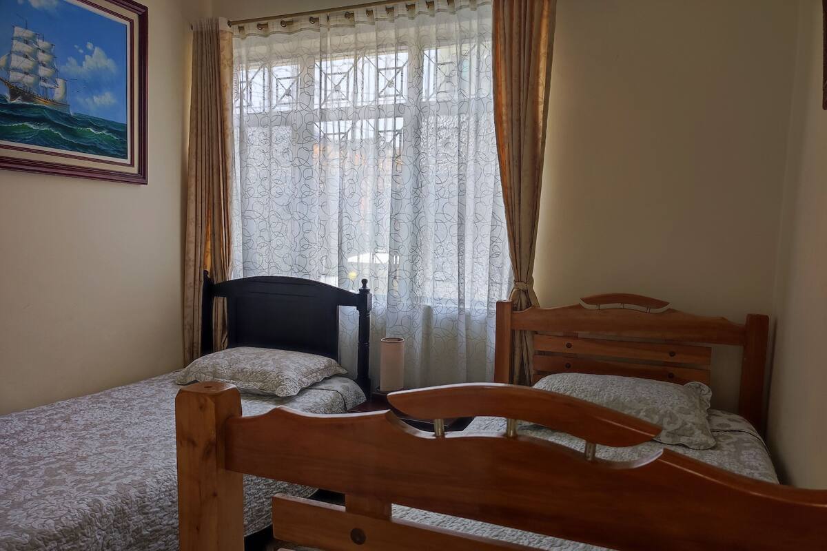 A bedroom with two wooden beds, a nightstand, a lamp, and a painting on the wall.