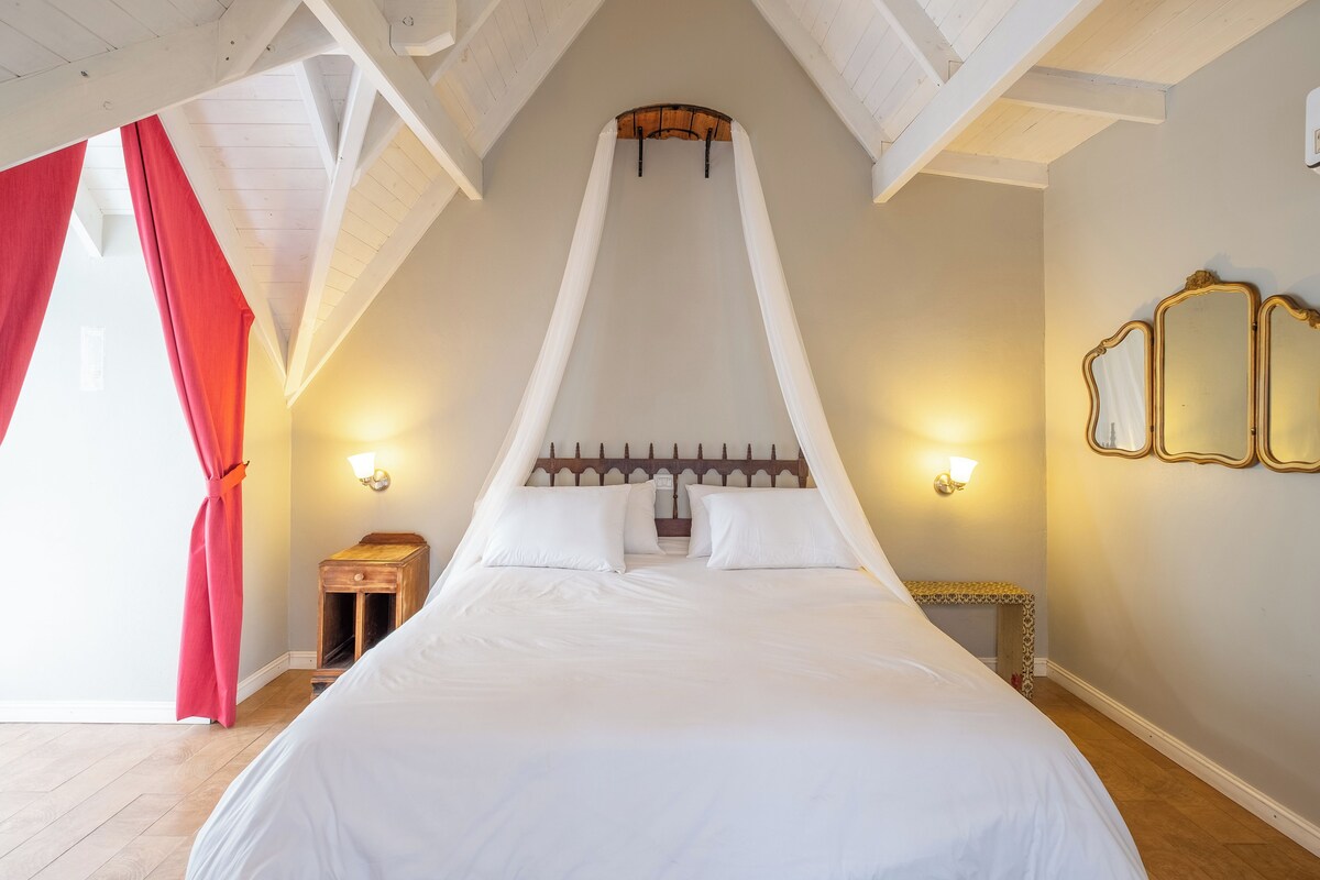 Un dormitorio con cama a dosel, lámparas de noche, una mesita y un espejo en la pared.