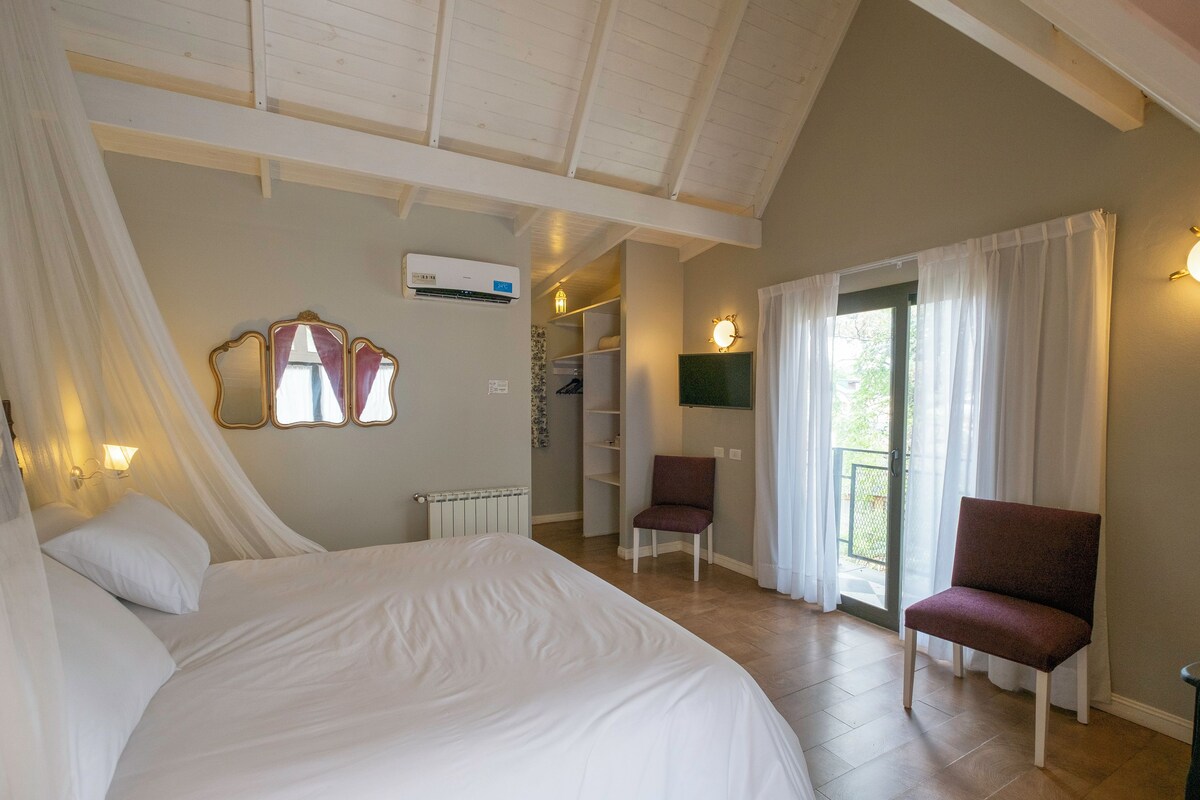 A bedroom with a large bed, a chair, a wardrobe, and a window with curtains.