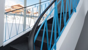 A staircase with a blue handrail and a glass balustrade, leading to a room with a view of snow-covered buildings.