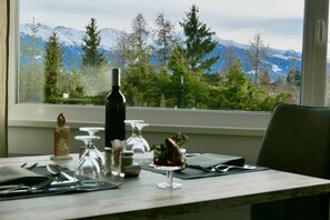 A dining table set with cutlery, a wine bottle, and a decorative item, with a mountain view through a window. - Hôtel Elite (Crans-Montana)