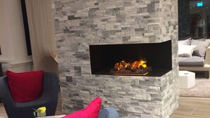A modern living room with a stone wall fireplace, grey upholstered armchairs, and a sofa with red cushions.