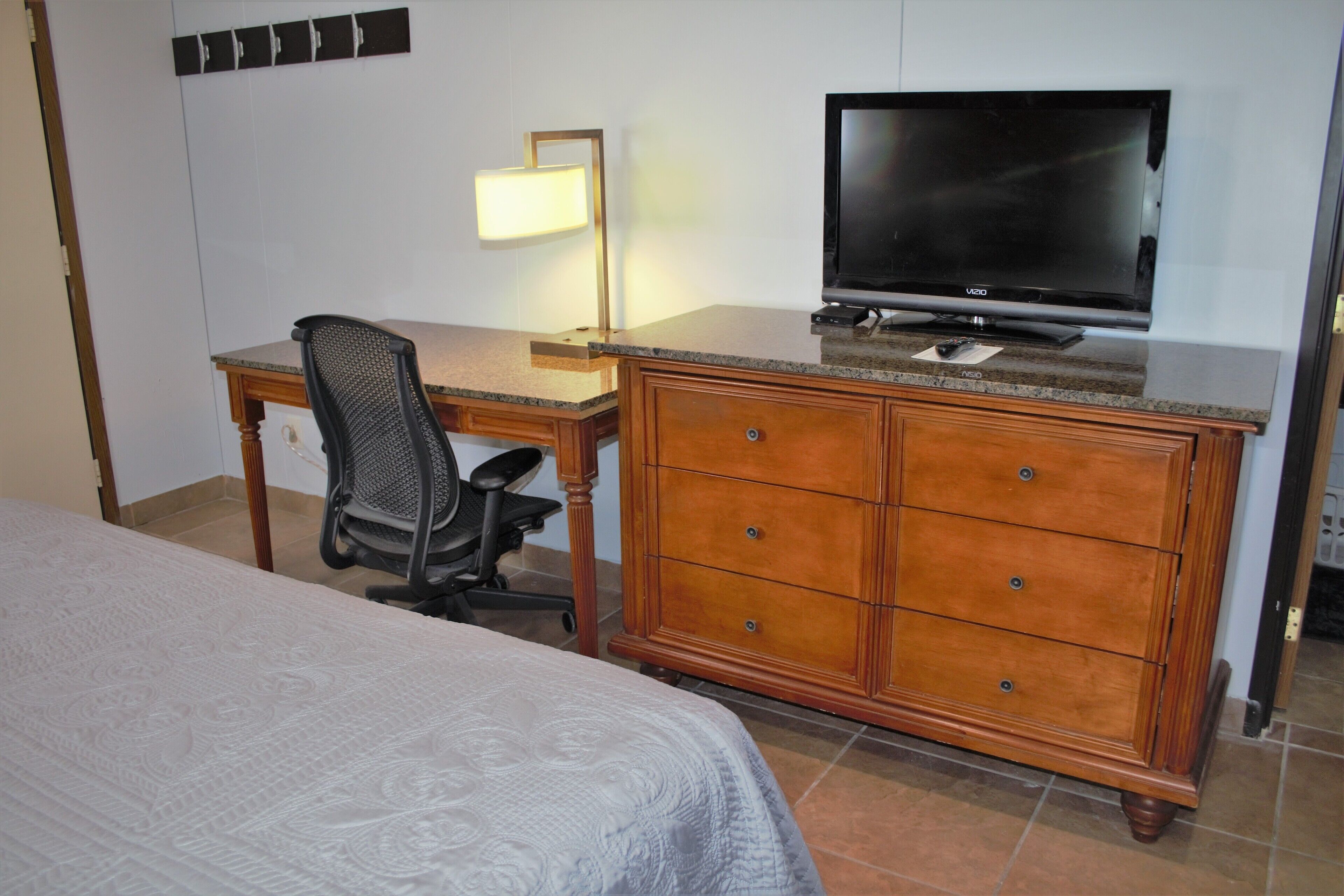Una habitación de hotel con una cama, un escritorio con televisor, una silla y un aparador.
