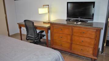 Una habitación de hotel con una cama, un escritorio con televisor, una silla y un aparador.