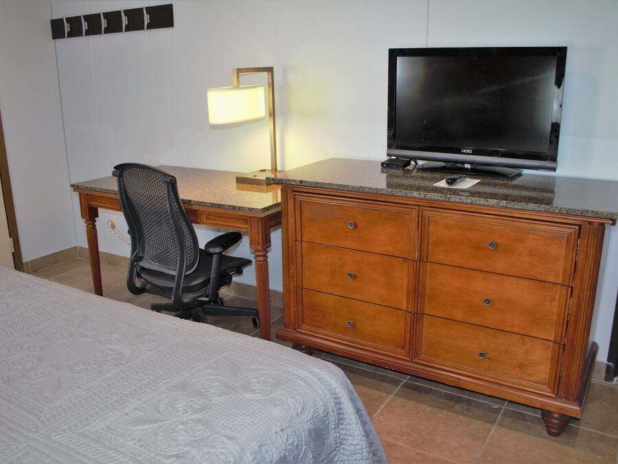 Una habitación de hotel con una cama, un escritorio con televisor, una silla y un aparador.