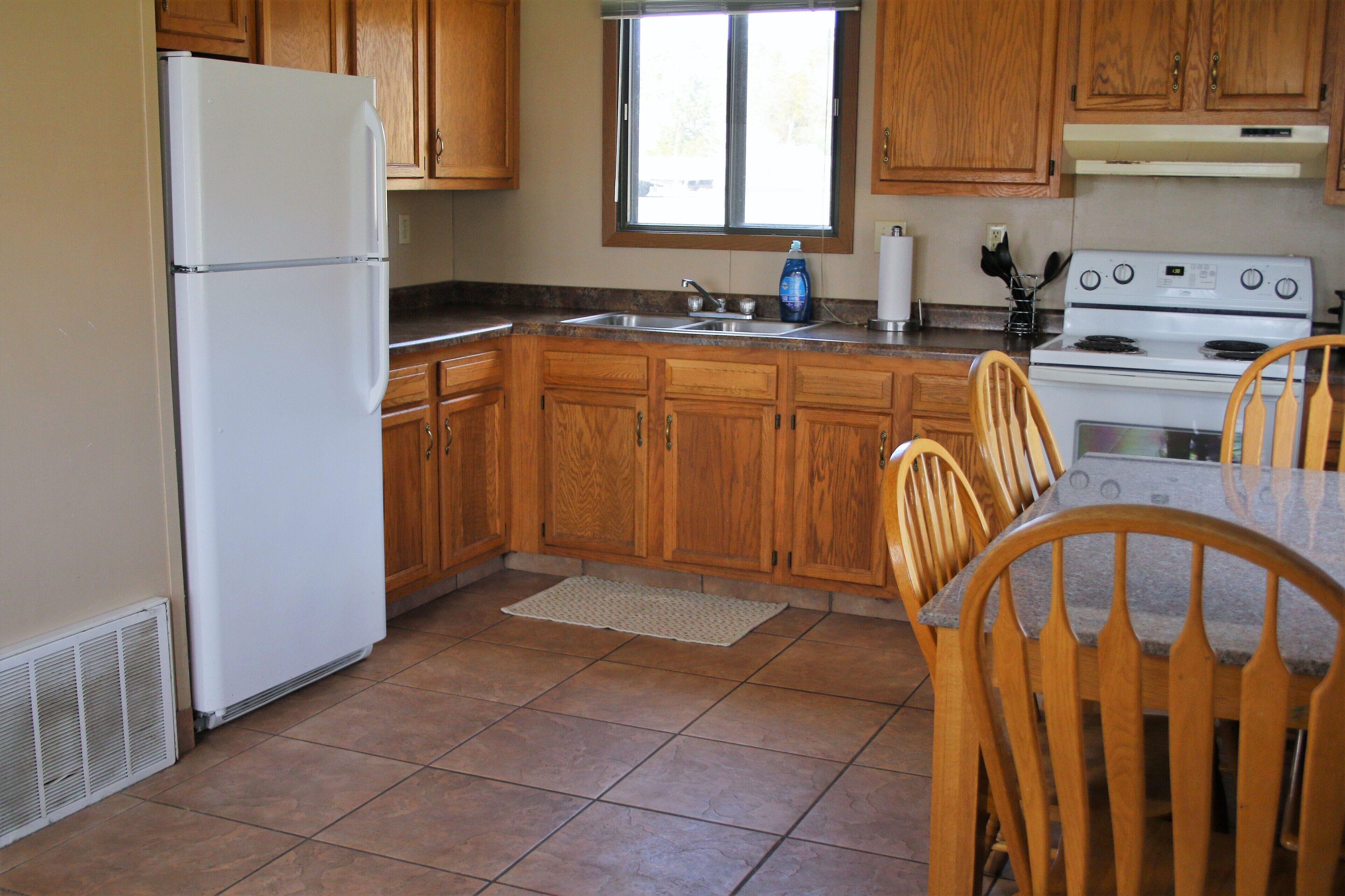 Una cocina con armarios de madera, un refrigerador blanco, una estufa y una mesa de comedor con sillas.