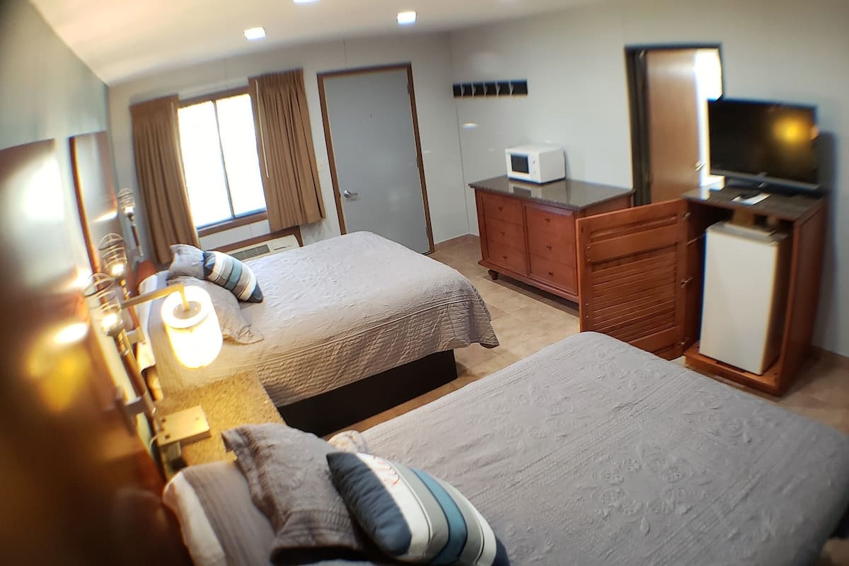 A hotel room with two beds, a TV, a microwave, and a refrigerator.