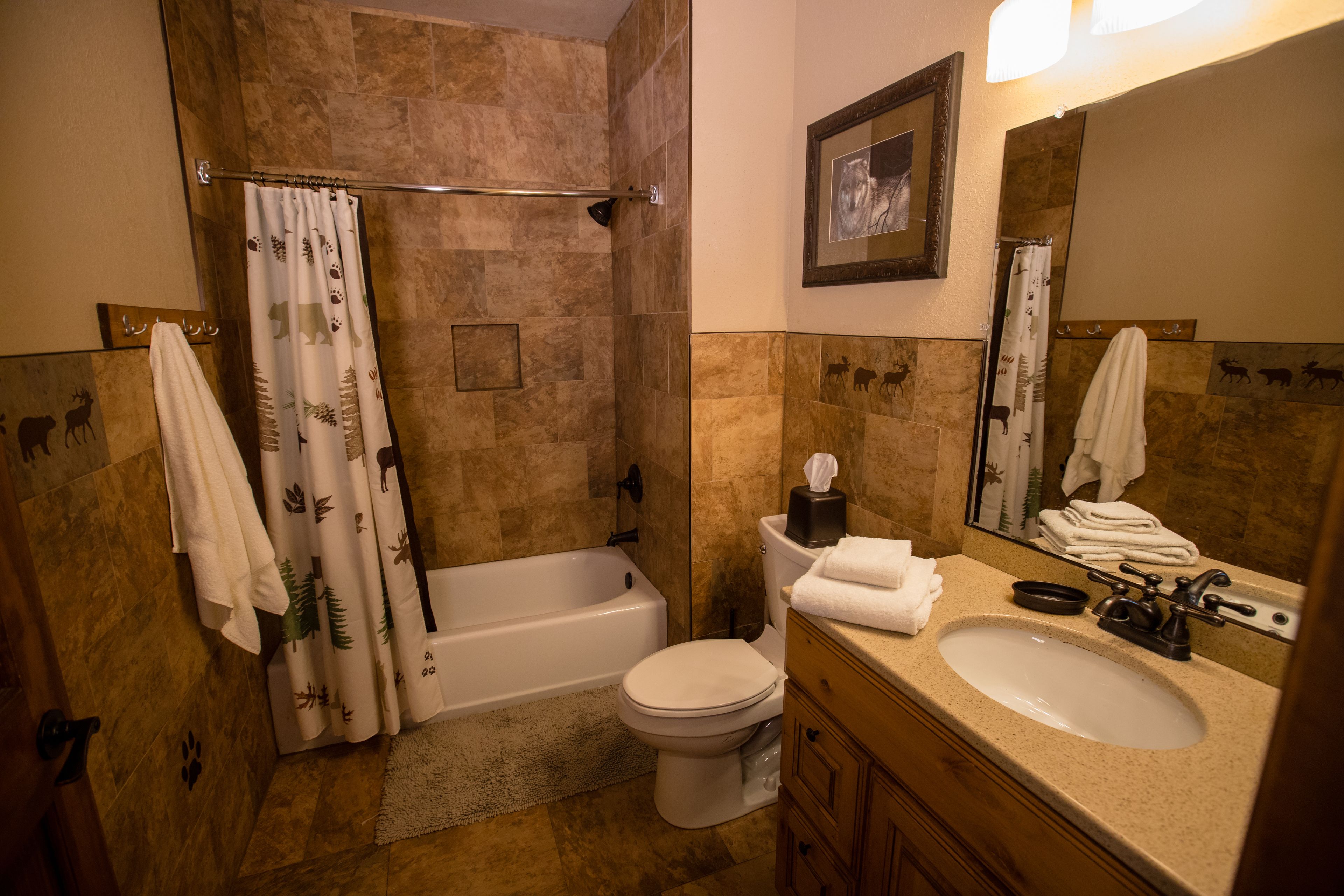 Un bagno con vasca, servizi igienici, lavandino e tenda da doccia con motivi animalier.