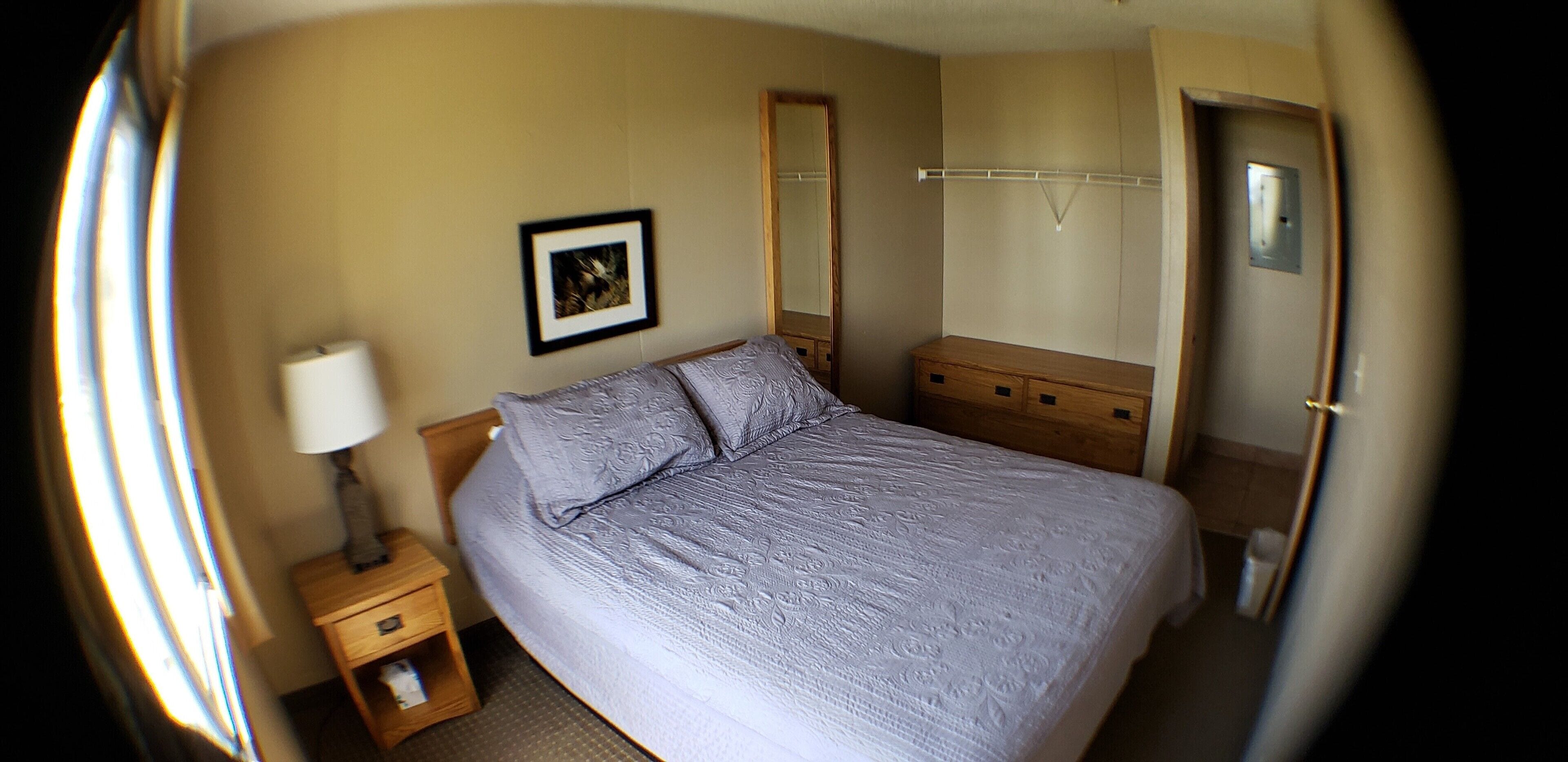 A bedroom with a bed, a bedside table with a lamp, a wardrobe, and a mirror.