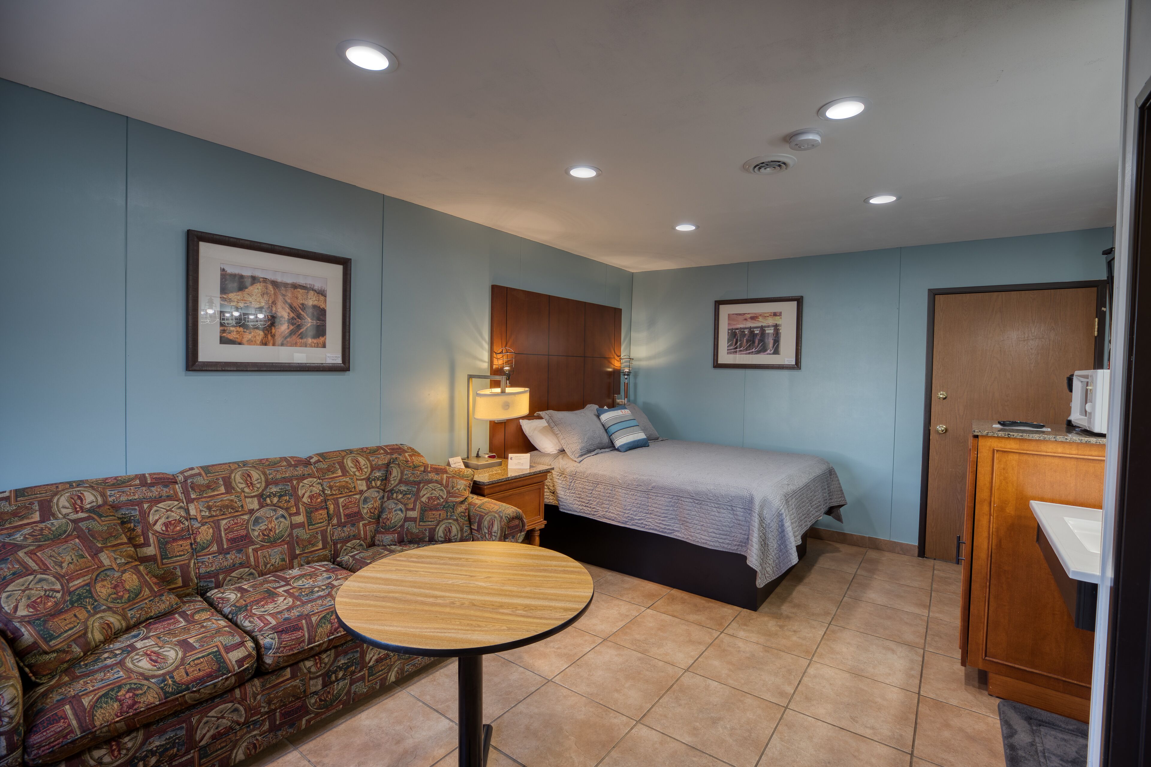 A hotel room with a sofa, a bed, a small round table, and a wooden cabinet.