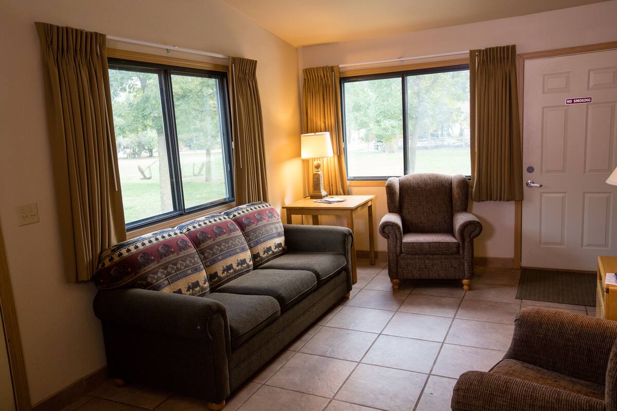 A living room with a sofa, armchair, and a small table with a lamp.