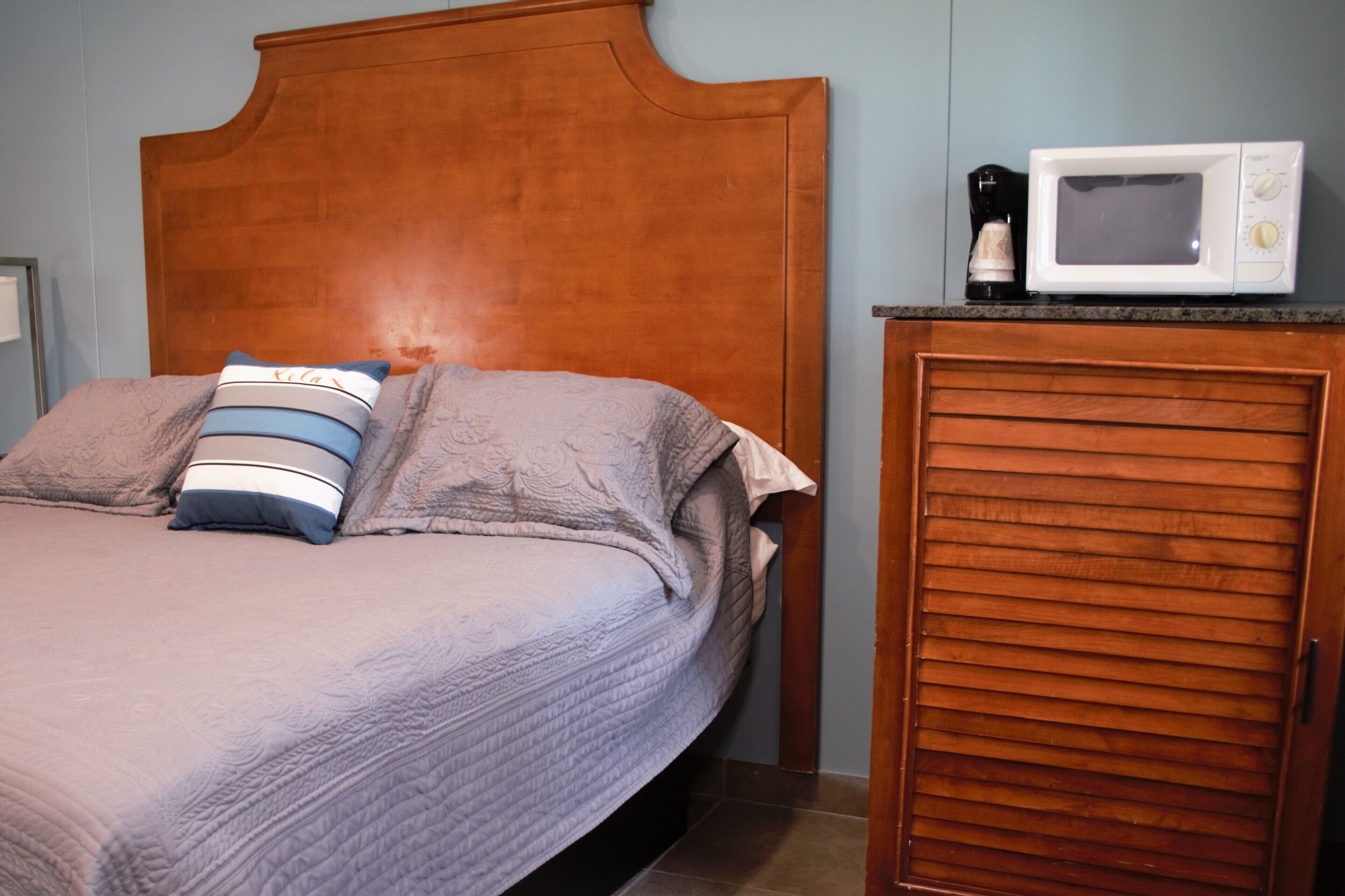 Una cama con cabecera de madera, una almohada y una manta. Hay un microondas sobre una encimera cerca de la cama.