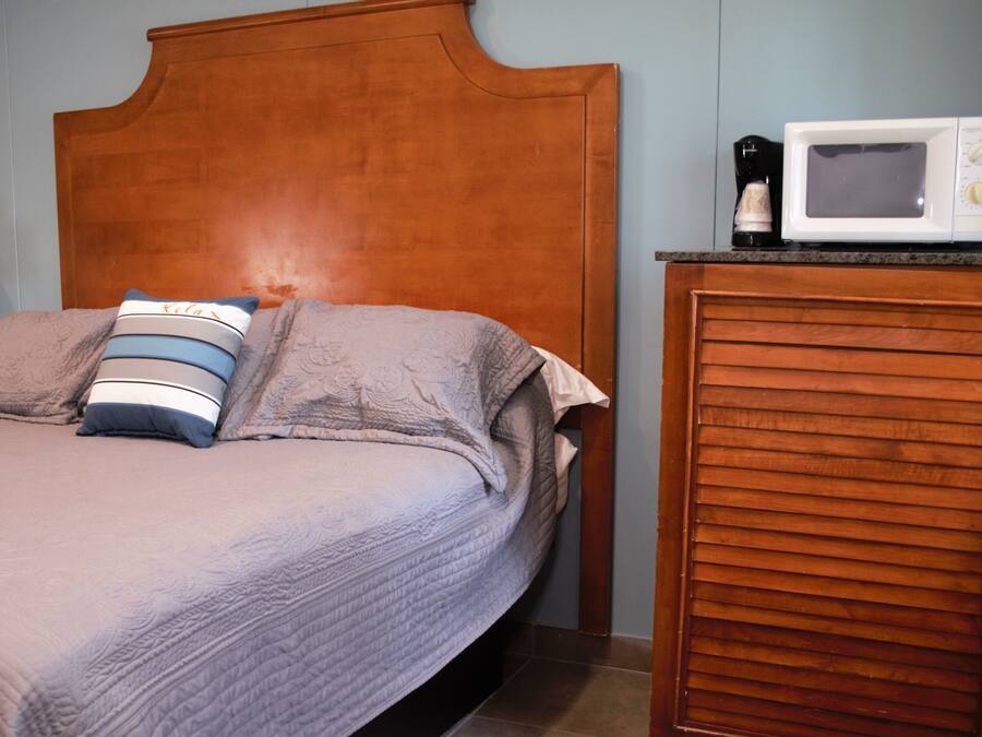 Una cama con cabecera de madera, una almohada y una manta. Hay un microondas sobre una encimera cerca de la cama.