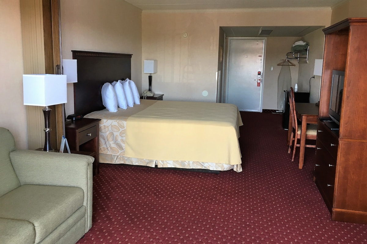 A hotel room with a bed, a desk, a chair, a lamp, and a wardrobe.