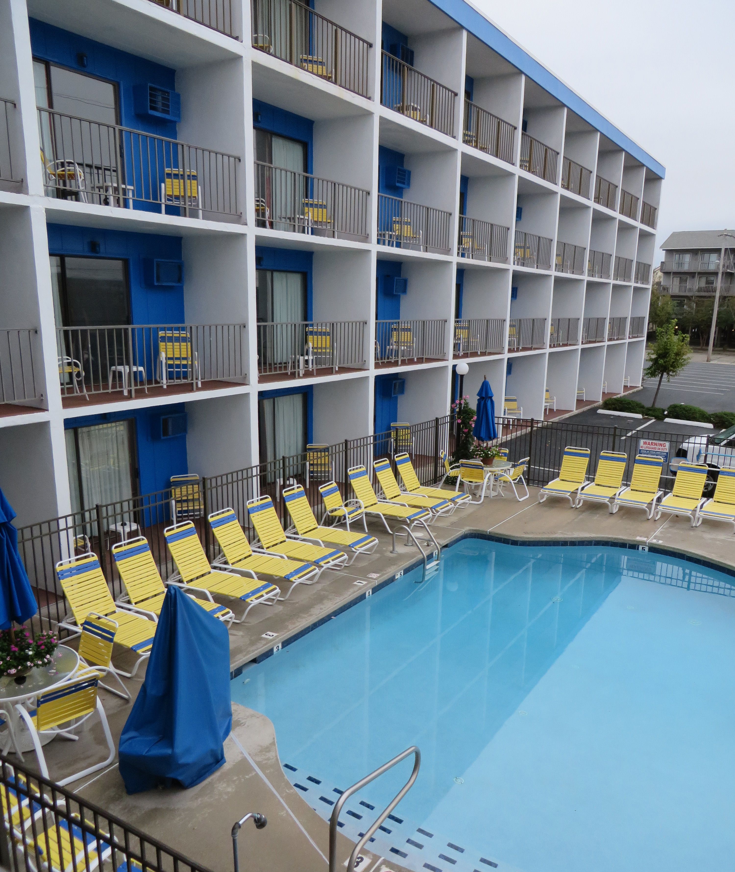 Un hôtel doté d’un espace piscine, de chaises longues jaunes et d’un auvent bleu.