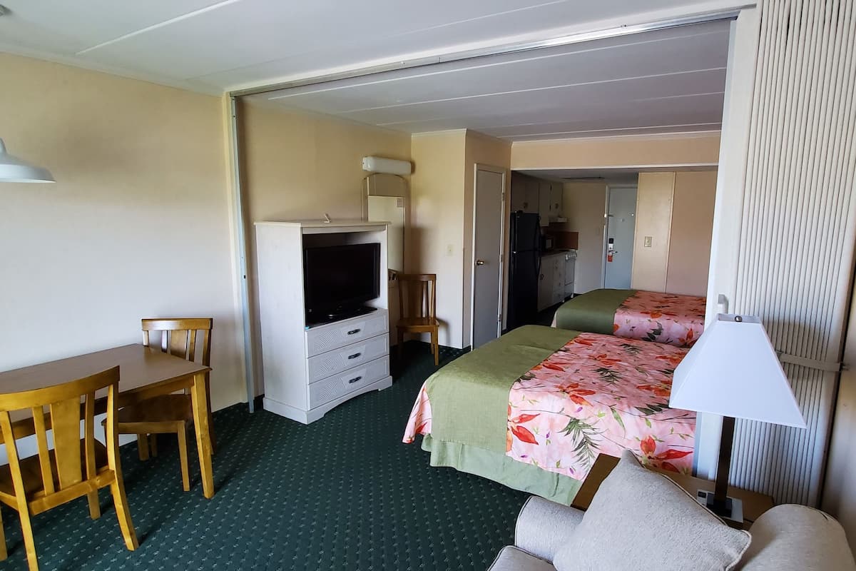 A compact hotel room with a single bed, a desk with a chair, a television, and a small kitchenette.