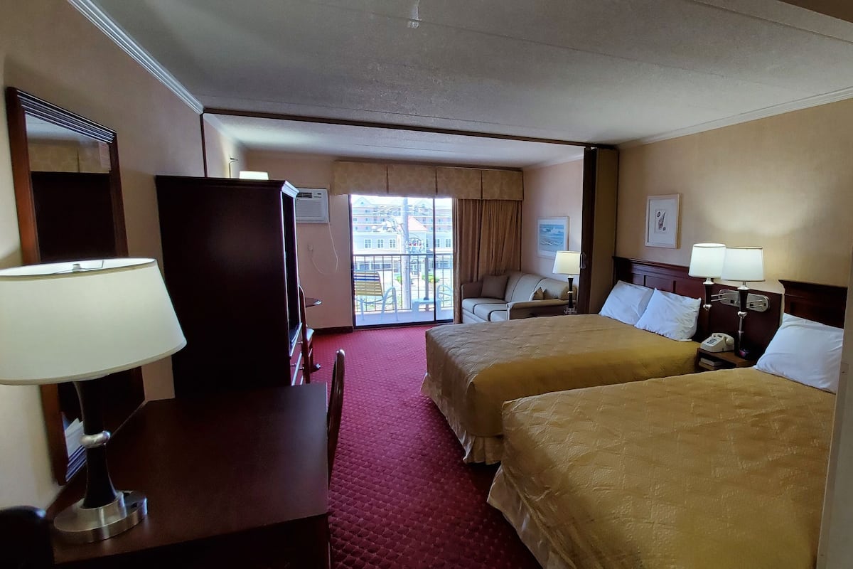 A hotel room with two beds, a desk, a chair, a TV, and a window with a view of buildings.