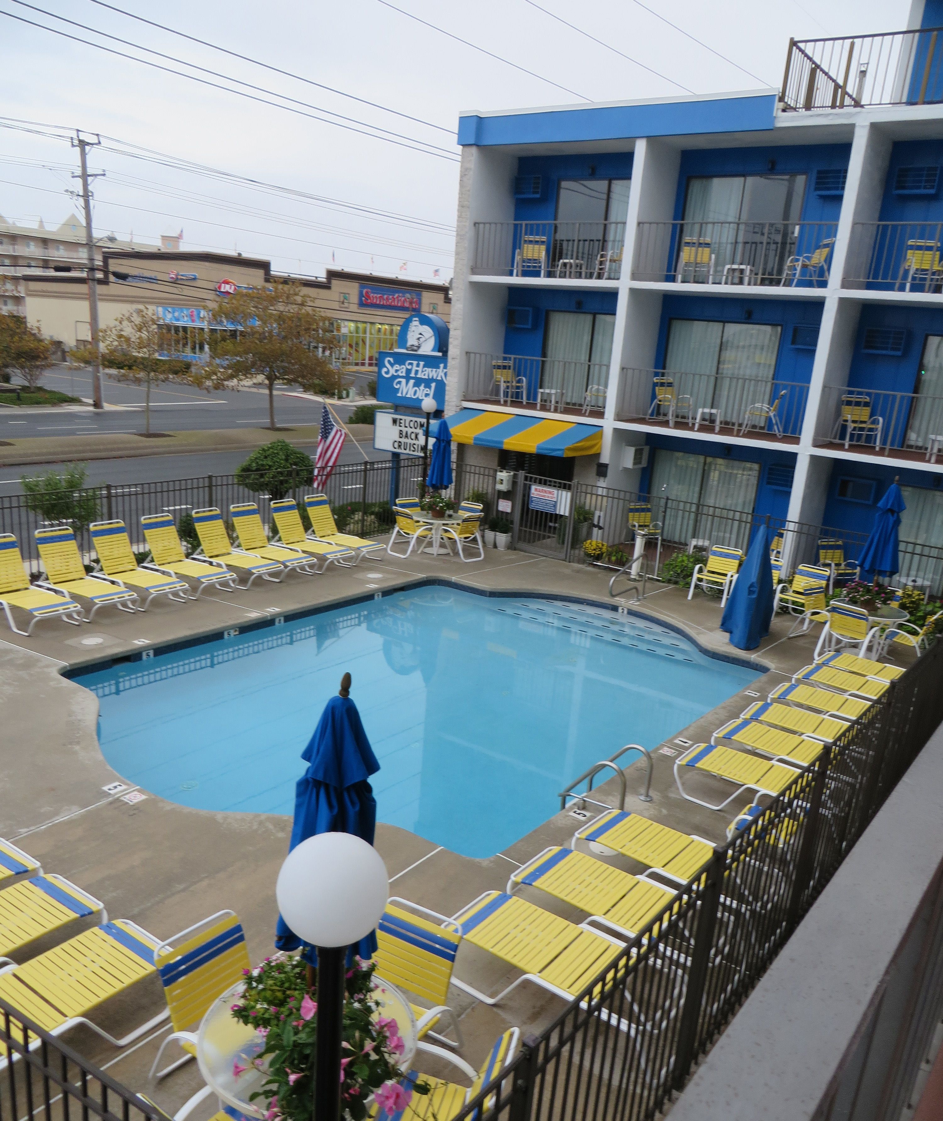 Un hôtel doté d’un espace piscine, de chaises longues jaunes et d’un auvent bleu et jaune.
